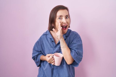 Téléchargez les photos : Moyen Age femme hispanique boire une tasse café main sur la bouche dire rumeur secrète, chuchoter conversation malicieuse - en image libre de droit
