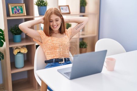 Téléchargez les photos : Jeune rousse femme en utilisant un ordinateur portable détendu avec les mains sur la tête à la maison - en image libre de droit