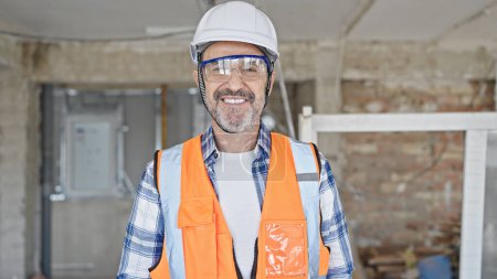 Téléchargez les photos : Moyen âge homme constructeur souriant confiance debout sur le chantier de construction - en image libre de droit