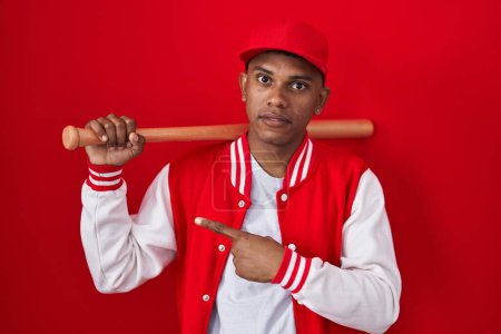 Photo for Young hispanic man playing baseball holding bat pointing aside worried and nervous with forefinger, concerned and surprised expression - Royalty Free Image