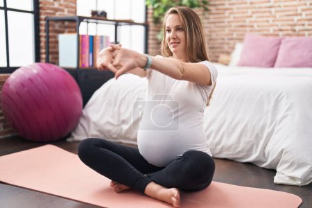 Photo for Young pregnant woman doing prepartum exercise sitting on yoga mat at bedroom - Royalty Free Image