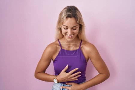 Téléchargez les photos : Young blonde woman standing over pink background smiling and laughing hard out loud because funny crazy joke with hands on body. - en image libre de droit