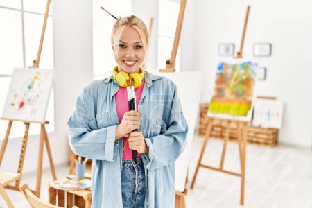 Téléchargez les photos : Jeune artiste caucasienne souriante confiante tenant pinceaux au studio d'art - en image libre de droit