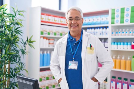 Téléchargez les photos : Homme moyen aux cheveux gris pharmacien souriant confiant debout à la pharmacie - en image libre de droit