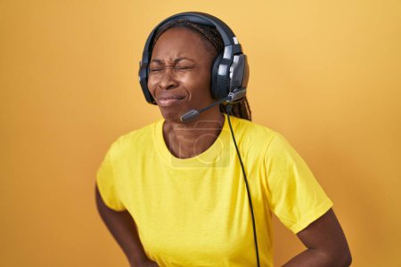 Photo for African american woman listening to music using headphones with hand on stomach because indigestion, painful illness feeling unwell. ache concept. - Royalty Free Image