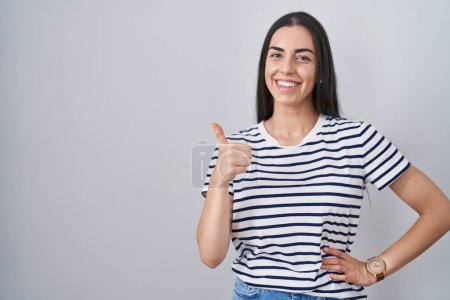 Téléchargez les photos : Jeune femme brune portant un t-shirt rayé faisant des pouces heureux geste avec la main. approuvant l'expression regardant la caméra montrant le succès. - en image libre de droit