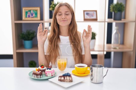 Photo for Young caucasian woman eating pastries t for breakfast relax and smiling with eyes closed doing meditation gesture with fingers. yoga concept. - Royalty Free Image