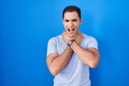 Photo for Young hispanic man standing over blue background shouting suffocate because painful strangle. health problem. asphyxiate and suicide concept. - Royalty Free Image