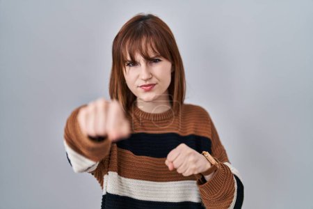 Photo for Young beautiful woman wearing striped sweater over isolated background punching fist to fight, aggressive and angry attack, threat and violence - Royalty Free Image