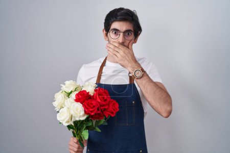 Foto de Un joven hispano sosteniendo un ramo de rosas blancas y rojas sorprendió cubriendo la boca con las manos por error. concepto secreto. - Imagen libre de derechos