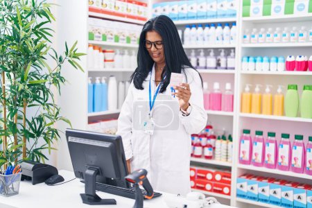 Téléchargez les photos : Moyen Age hispanique femme pharmacien tenant comprimés pilule à l'aide d'un ordinateur à la pharmacie - en image libre de droit