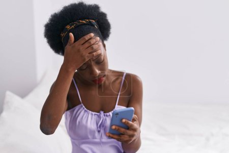 Foto de African american woman using smartphone with serious expression at bedroom - Imagen libre de derechos