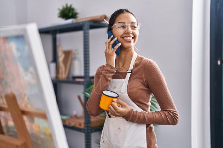 Photo for Young african american woman artist talking on the smartphone drinking coffee at art studio - Royalty Free Image