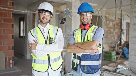 Téléchargez les photos : Deux hommes constructeurs souriant confiants debout avec les bras croisés geste sur le chantier de construction - en image libre de droit