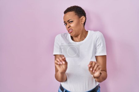 Photo for Beautiful african american woman standing over pink background disgusted expression, displeased and fearful doing disgust face because aversion reaction. - Royalty Free Image