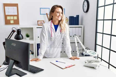Foto de Young woman wearing doctor uniform smiling confident standing at clinic - Imagen libre de derechos