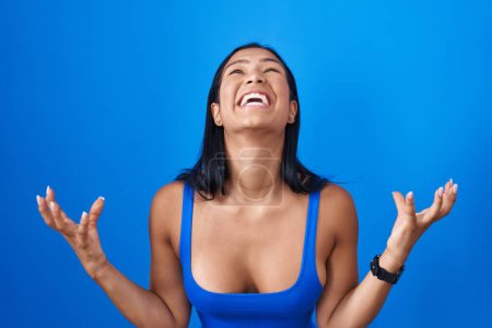 Photo for Hispanic woman standing over blue background crazy and mad shouting and yelling with aggressive expression and arms raised. frustration concept. - Royalty Free Image