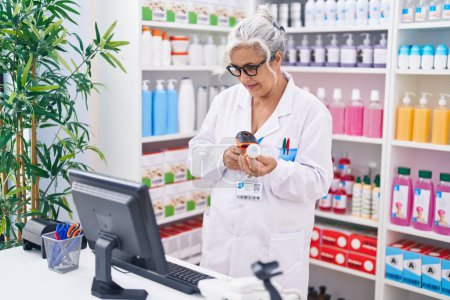 Foto de Mujer de pelo gris de mediana edad farmacéutica que escanea la botella de pastillas en la farmacia - Imagen libre de derechos
