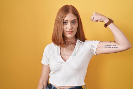 Téléchargez les photos : Jeune rousse femme debout sur fond jaune personne forte montrant muscle du bras, confiant et fier de la puissance - en image libre de droit