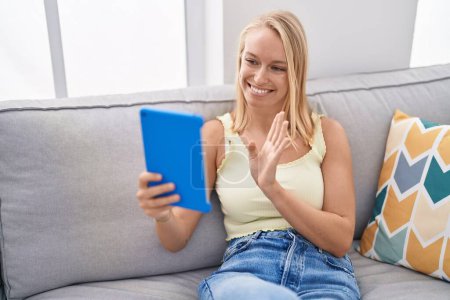 Photo for Young caucasian woman using touchpad sitting on the sofa looking positive and happy standing and smiling with a confident smile showing teeth - Royalty Free Image