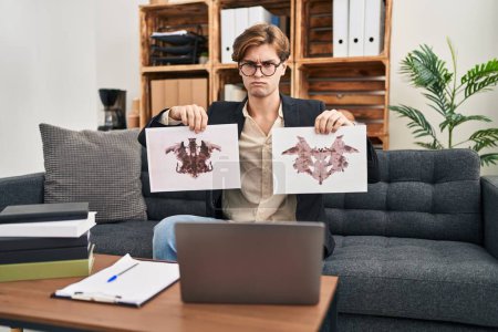 Photo for Young therapist man working with rorschach test at psychology clinic skeptic and nervous, frowning upset because of problem. negative person. - Royalty Free Image