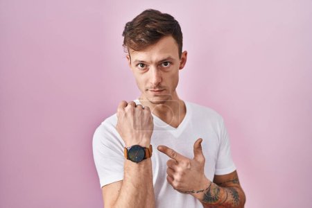 Photo for Caucasian man standing over pink background in hurry pointing to watch time, impatience, looking at the camera with relaxed expression - Royalty Free Image