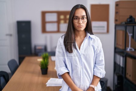 Photo for Young hispanic woman at the office relaxed with serious expression on face. simple and natural looking at the camera. - Royalty Free Image