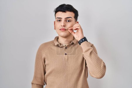 Photo for Non binary person standing over isolated background mouth and lips shut as zip with fingers. secret and silent, taboo talking - Royalty Free Image