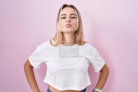 Photo for Young blonde woman standing over pink background looking at the camera blowing a kiss on air being lovely and sexy. love expression. - Royalty Free Image