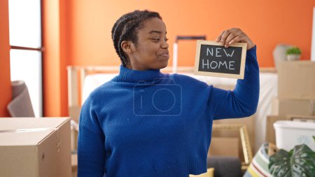 Téléchargez les photos : Afro-américaine femme souriant confiant tenant tableau noir à la nouvelle maison - en image libre de droit
