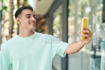Foto de Young hispanic man smiling confident making selfie by the smartphone at street - Imagen libre de derechos