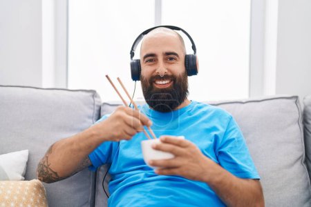 Photo for Young bald man listening to music eating chinese food at home - Royalty Free Image