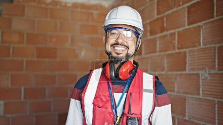 Téléchargez les photos : Jeune homme latino constructeur souriant confiance debout sur le chantier de construction - en image libre de droit