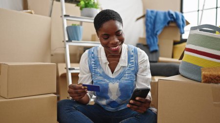 Foto de Mujer afroamericana de compras con teléfono inteligente y tarjeta de crédito en un nuevo hogar - Imagen libre de derechos