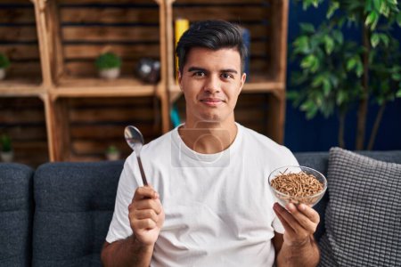 Photo for Hispanic man eating healthy whole grain cereals with spoon relaxed with serious expression on face. simple and natural looking at the camera. - Royalty Free Image
