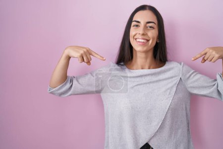 Photo for Young brunette woman standing over pink background looking confident with smile on face, pointing oneself with fingers proud and happy. - Royalty Free Image