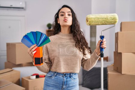 Photo for Young brunette woman moving to a new home painting walls looking at the camera blowing a kiss being lovely and sexy. love expression. - Royalty Free Image