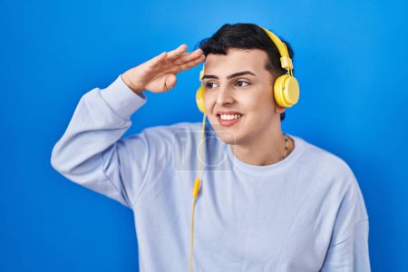 Téléchargez les photos : Personne non binaire écoutant de la musique à l'aide d'écouteurs très heureux et souriant regardant loin avec la main sur la tête. concept de recherche. - en image libre de droit