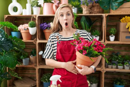 Photo for Young caucasian woman working at florist shop holding plant scared and amazed with open mouth for surprise, disbelief face - Royalty Free Image