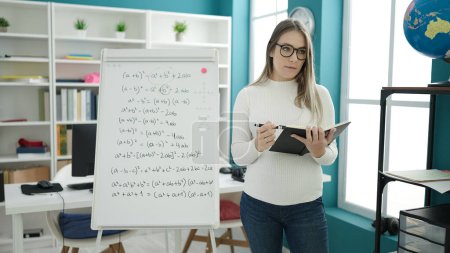 Photo for Young pregnant woman teaching maths on magnetic board reading book at classroom - Royalty Free Image