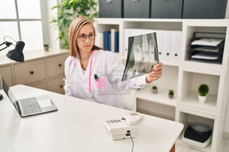 Téléchargez les photos : Jeune femme blonde médecin à l'aide d'un ordinateur portable tenant rayons X à la clinique - en image libre de droit