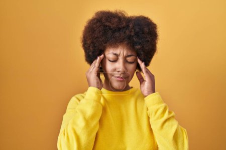 Téléchargez les photos : Jeune femme afro-américaine debout sur fond jaune avec la main sur la tête pour la douleur à la tête parce que le stress. migraine souffrant. - en image libre de droit