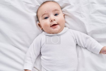 Téléchargez les photos : Adorable bébé souriant confiant couché sur le lit dans la chambre - en image libre de droit
