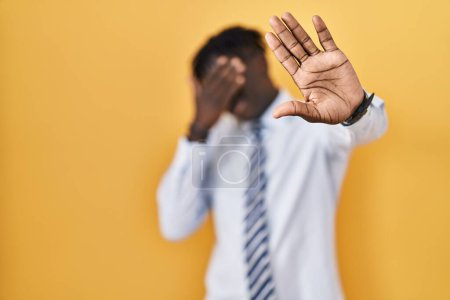 Téléchargez les photos : Homme africain avec dreadlocks debout sur fond jaune couvrant les yeux avec les mains et faire arrêter geste avec expression triste et peur. concept embarrassé et négatif. - en image libre de droit