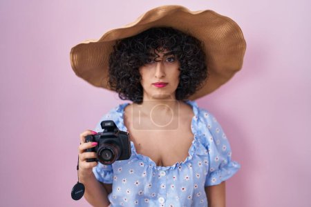 Photo for Young brunette woman with curly hair using reflex camera thinking attitude and sober expression looking self confident - Royalty Free Image