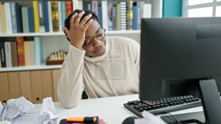 Foto de African american woman student using computer stressed at library university - Imagen libre de derechos