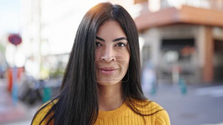 Téléchargez les photos : Jeune belle femme hispanique debout avec une expression détendue dans la rue - en image libre de droit