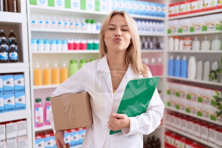 Photo for Young caucasian woman working at pharmacy drugstore holding box doing inventory looking at the camera blowing a kiss being lovely and sexy. love expression. - Royalty Free Image