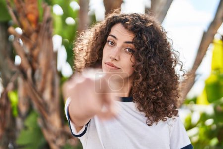 Photo for Hispanic woman with curly hair standing outdoors pointing with finger to the camera and to you, confident gesture looking serious - Royalty Free Image