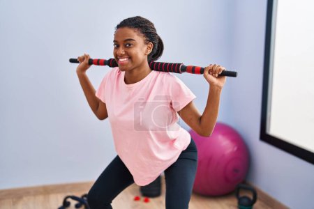 Foto de Mujer afroamericana sonriendo con confianza ejercicio piernas de entrenamiento en el centro deportivo - Imagen libre de derechos